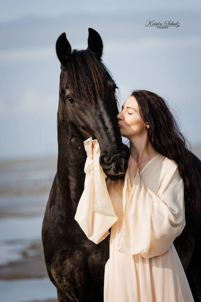 Eine Frau steht neben ihrem Pferd und küsst und streichelt es liebevoll.